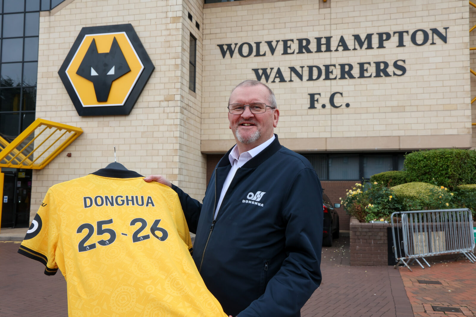 Wolves Business Partner - Bob Wellsbury standing outside stadium holding Donghua branded football shirt