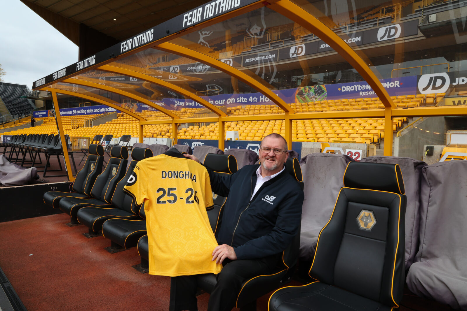 Wolves Business Partner Bob Wellsbury sitting in dug out holding Donghua branded football shirt